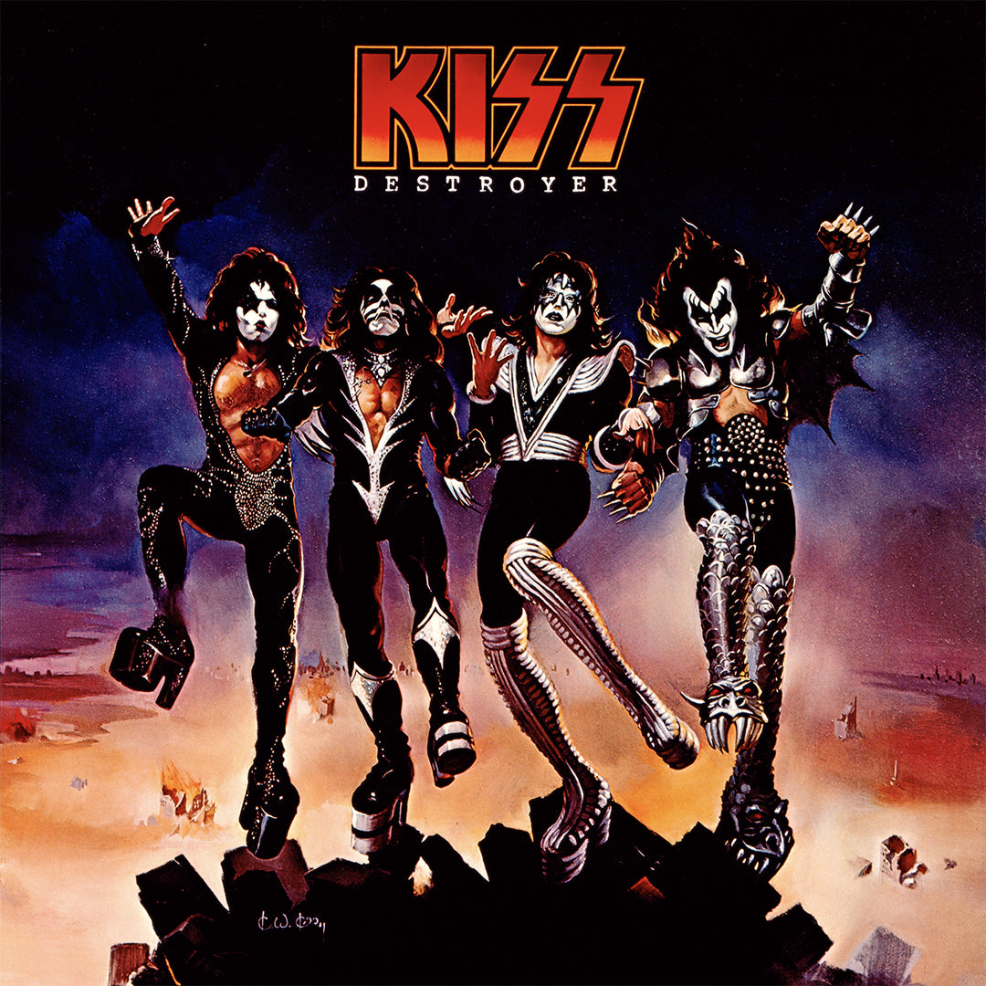 KISS in their iconic platform shoes and black & silver jumpsuits with a desert landscape background.